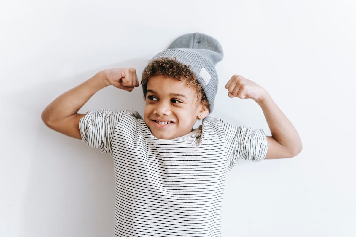 Happy boy flexing his muscles, illustrating how to empower strong-willed children to listen.