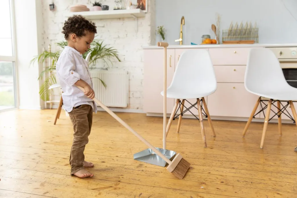 A little boy sweeping the kitchen floor with child-size broom and dustpan
