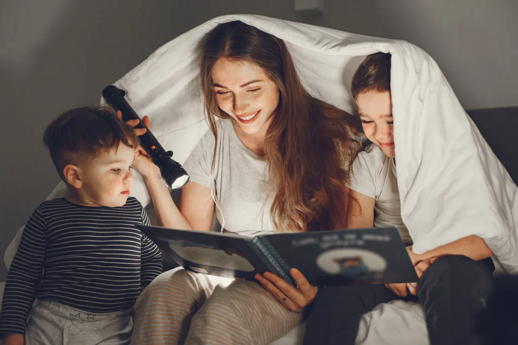 Young mother reading to sons under the covers using a flashlight