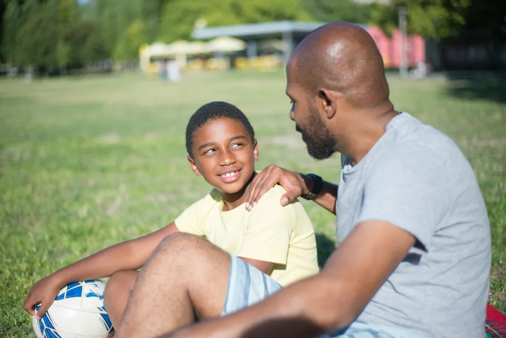 Father and son having a conversation while sitting on the grass on the football court