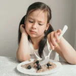 Girl with disgusted grimace doesn’t want to eat porridge