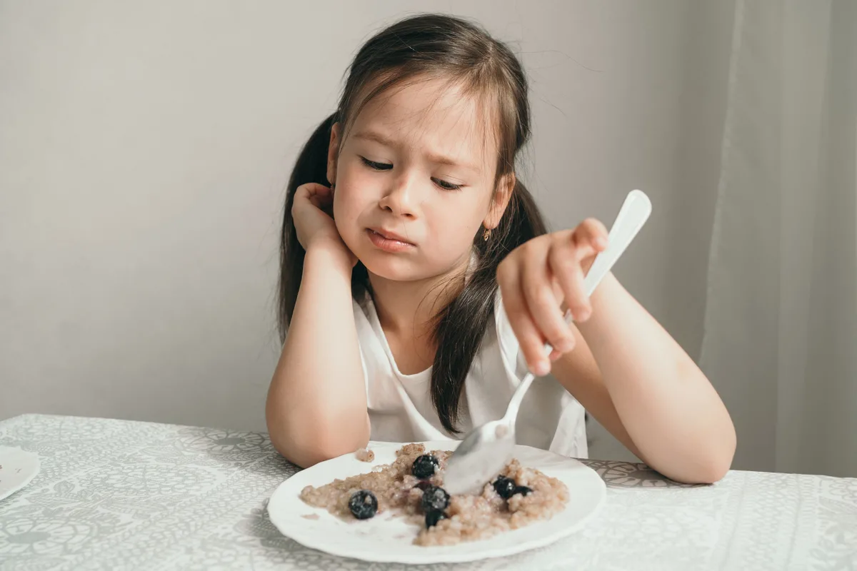 Girl with disgusted grimace doesn’t want to eat porridge