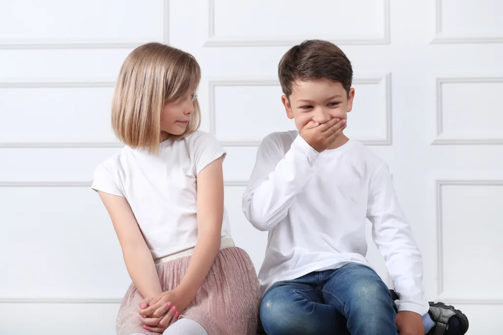 why do children lie - A girl looks unimpressed at a boy covering his mouth and laughing