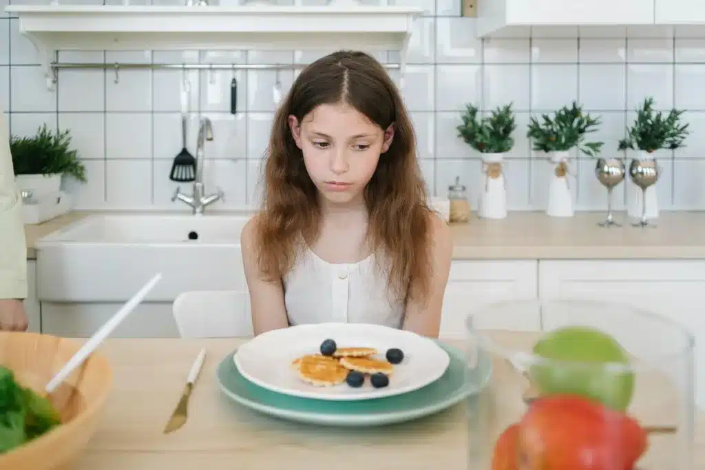 how to get a child to eat when they refuse - Sad young girl at the table looking away from her plate