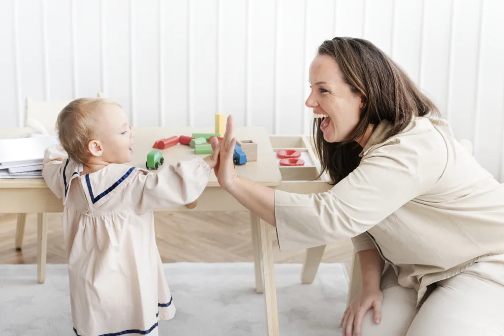 Toddler giving high five to knealed smiling care taker at daycare