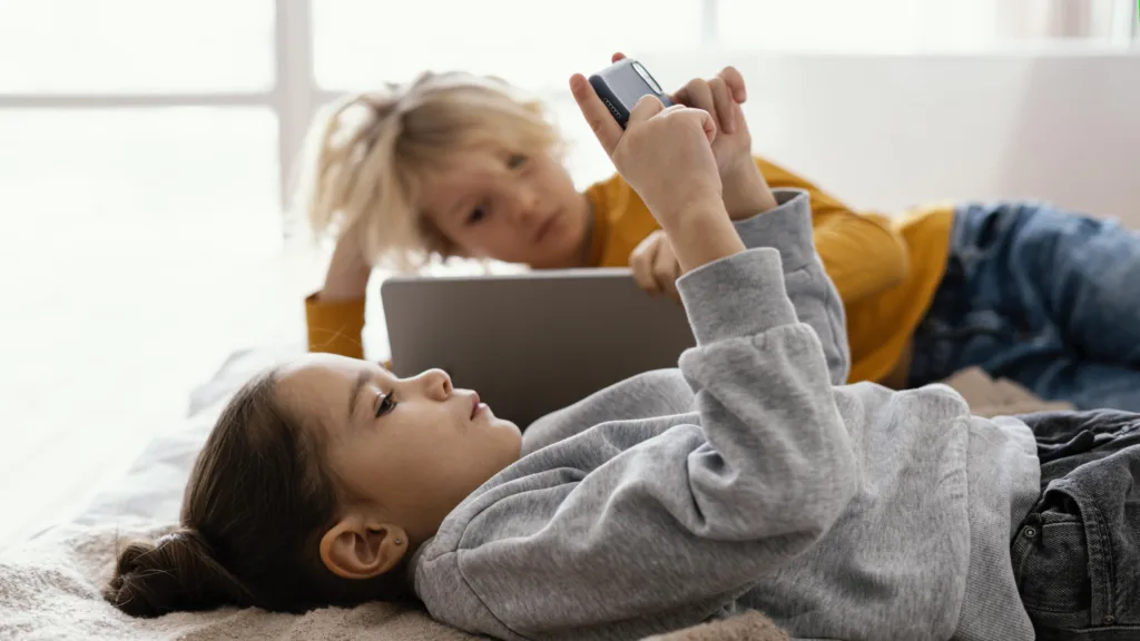 Siblings on the bed using a smartphone and a laptop