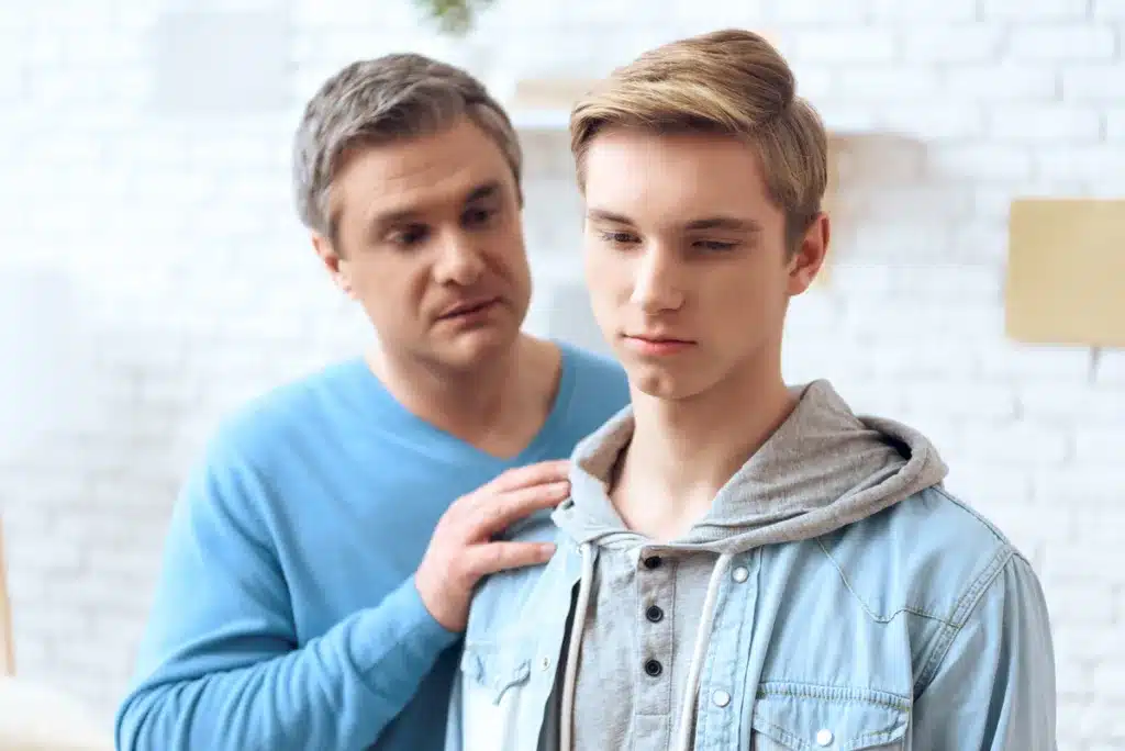 Father touching his son’s shoulder trying to communicate while son looks away