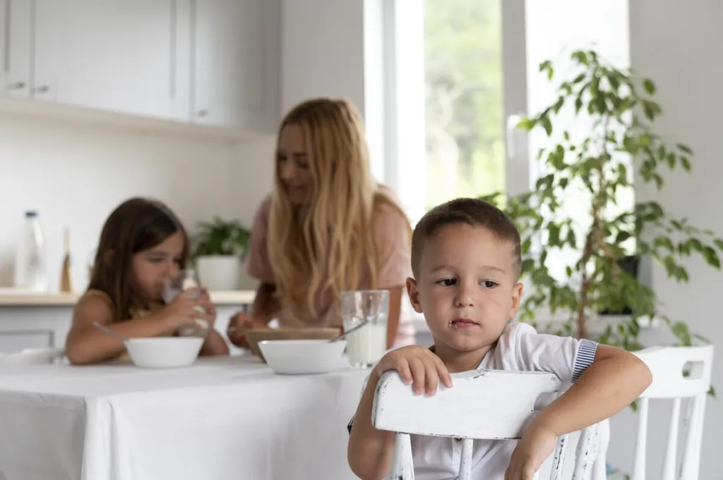 Mother spending time with daughter at the table while son looks away with back turned to them