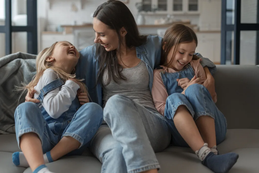 Mom holding her two daughters, having a good time laughing on the sofa