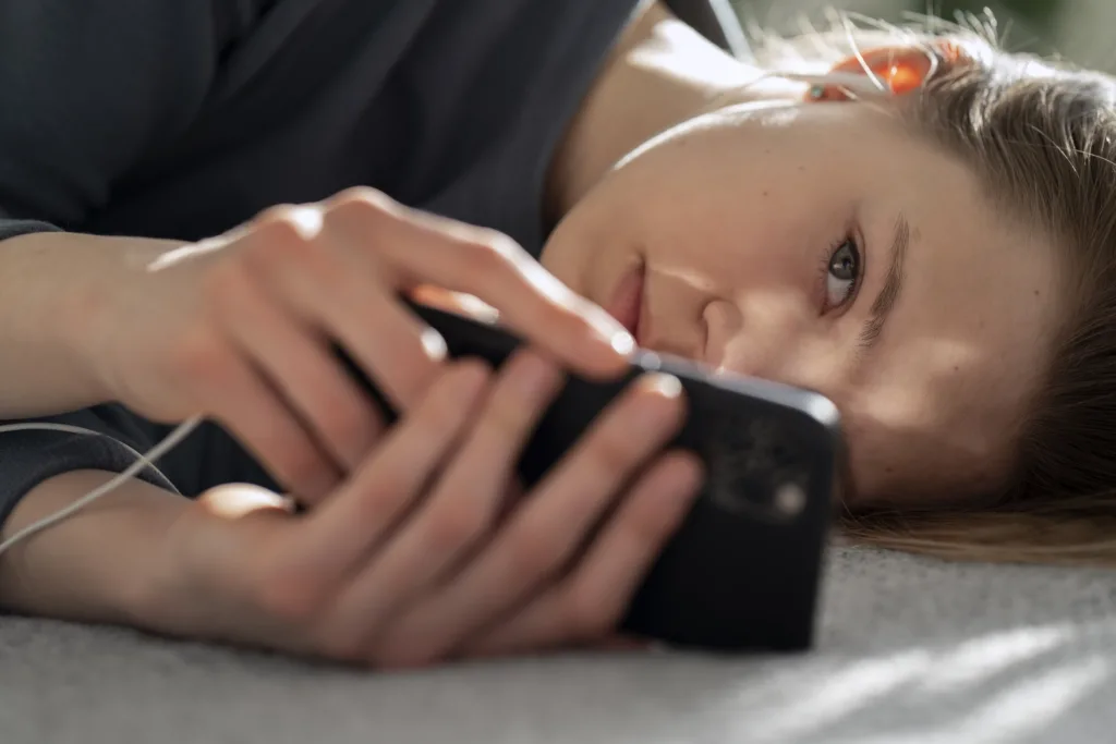 Teen with headphones sitting on the bed holding a  smartphone