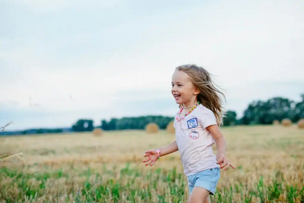 Young girl with a beaming smile, joyfully running across a vibrant green field, expressing pure happiness 