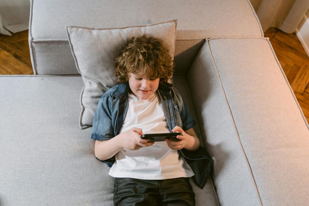 A boy sitting on a couch, focused on playing with his phone.