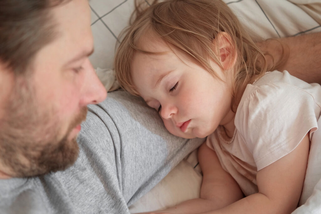 Dad lovingly looking at his daughter while she sleeps on his arm