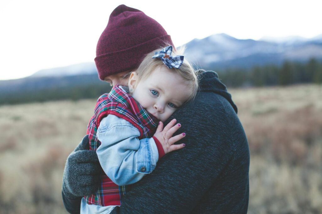 Dad holding little girl in his arms outdoors, sharing a loving moment in nature.