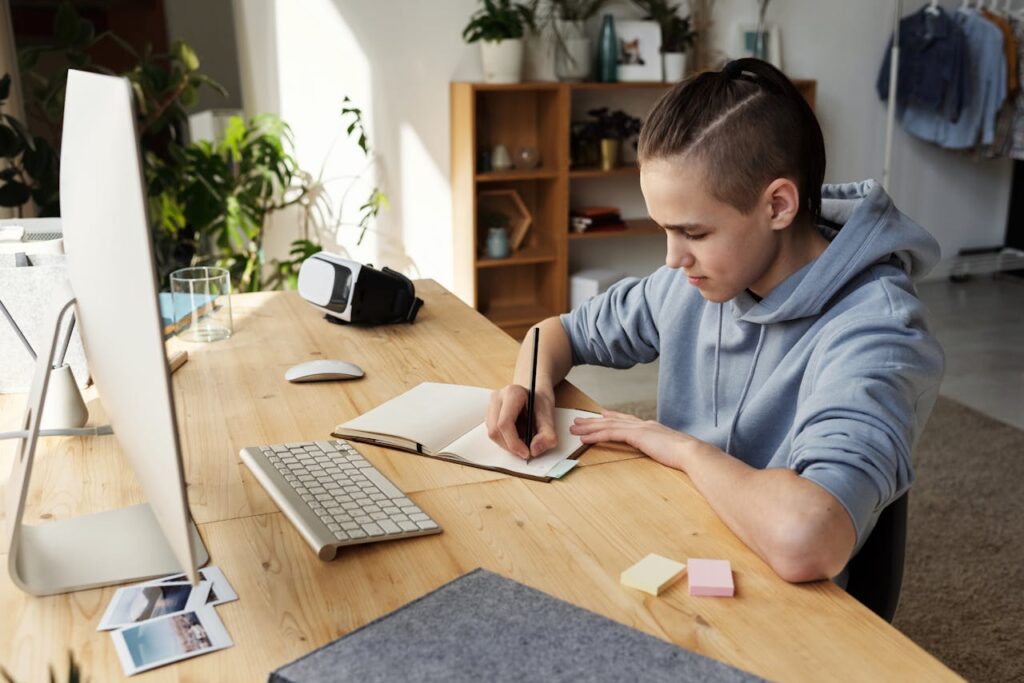 A preteen boy sitting at a desk, writing homework, while home alone.