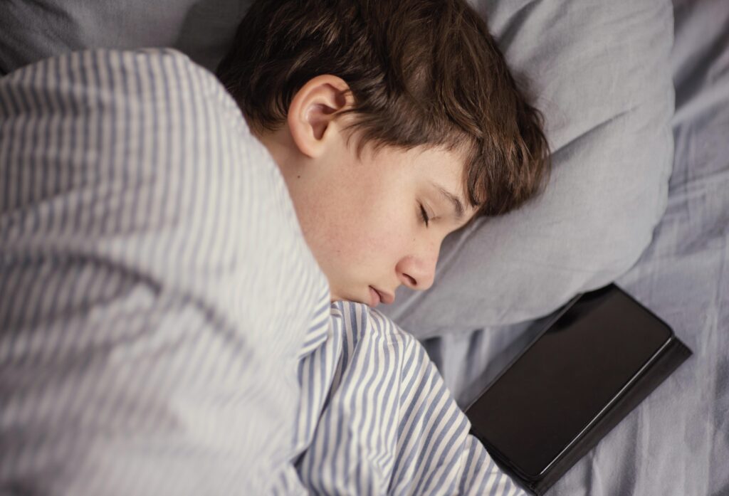 Teen boy asleep with a smartphone beside him