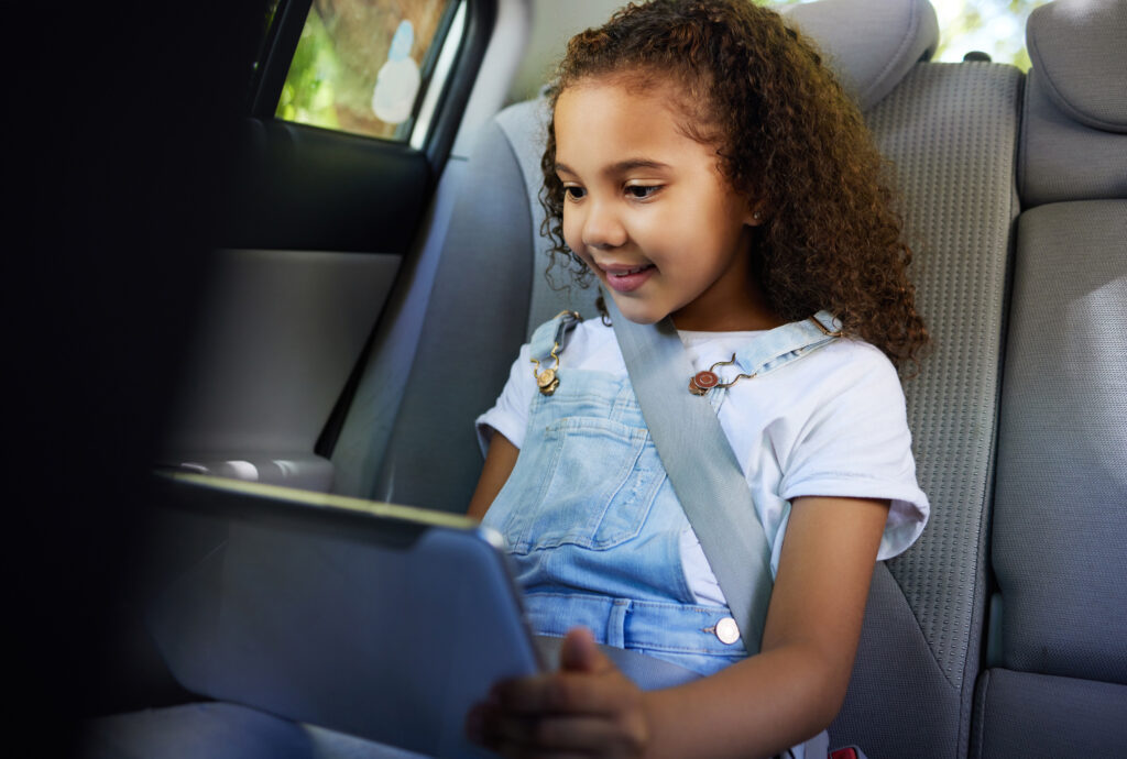 Smiling girl in the backseat of a car watching a video on the tablet
