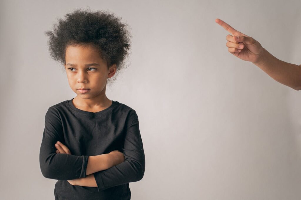 An upset boy is being scolded by a parent, with the parent's index finger visible in the picture.