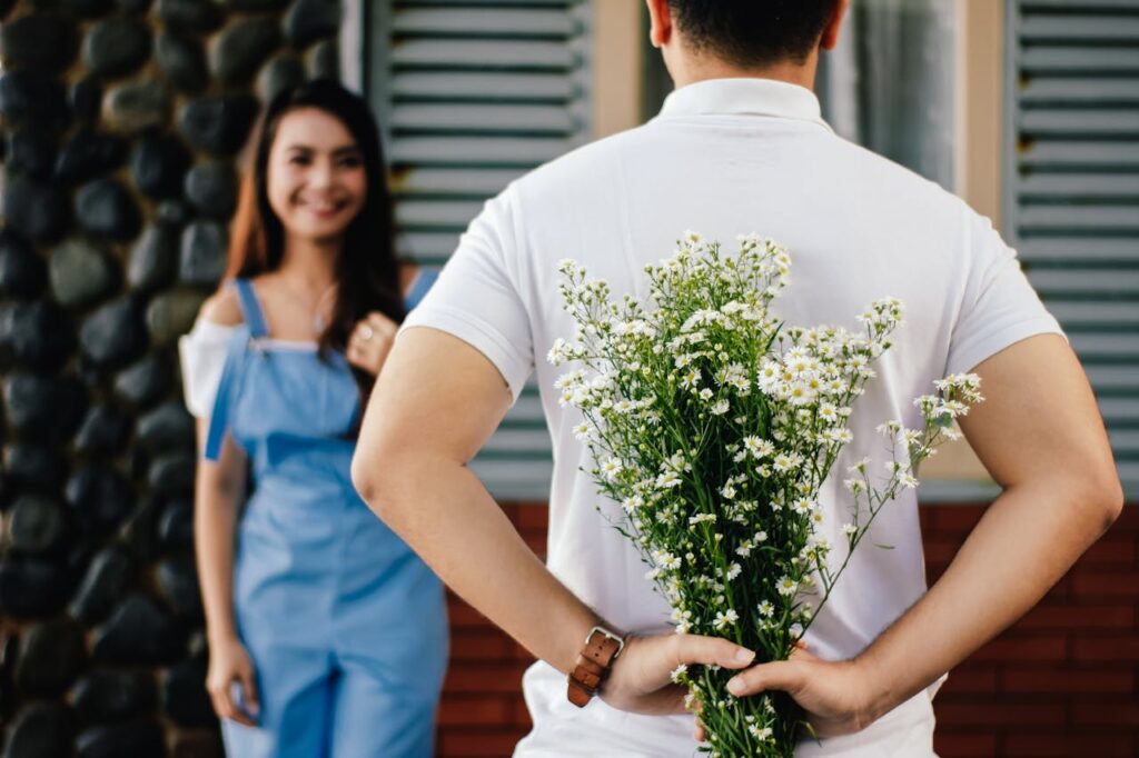 A teenage boy hides a bouquet of flowers behind his back, preparing to surprise his teen girlfriend