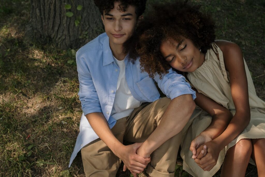 A teenage couple stands close together, the girl resting her head on her boyfriend's shoulder, sharing a tender and intimate moment.