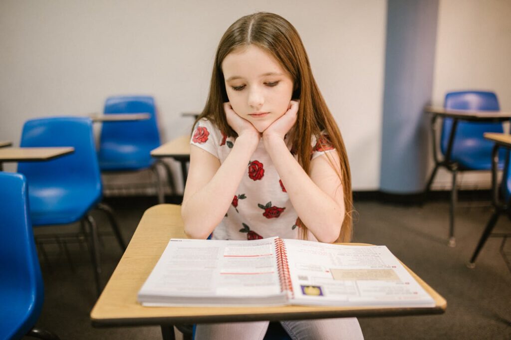 School-aged girl at her desk looking upset at her book.