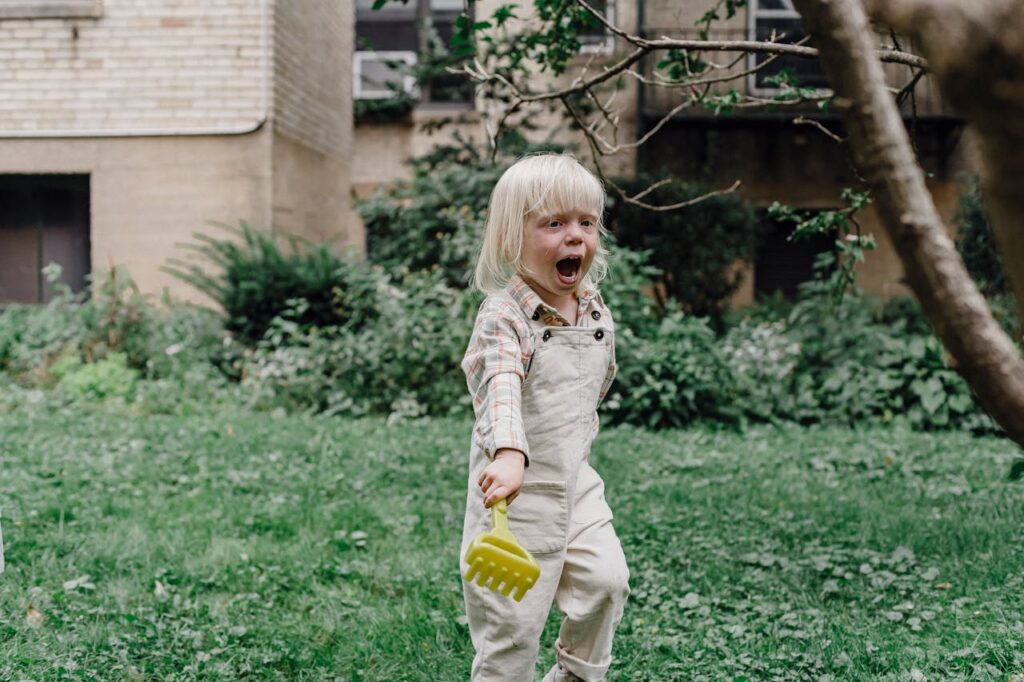 A little boy crying and shouting in a yard, showing signs of a tantrum.