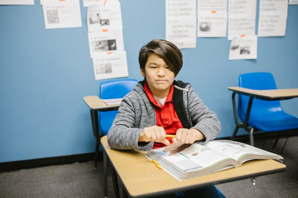 An angry boy at school breaking a pencil in frustration.