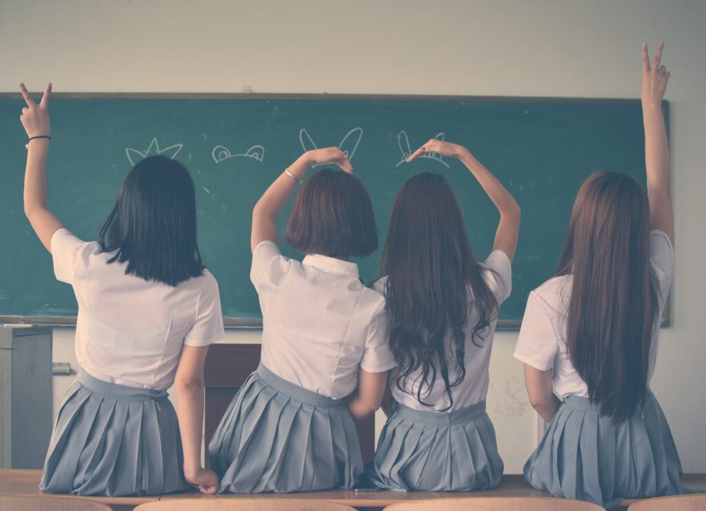 View from the back of four little girls standing on a desk, looking at the board in the classroom.