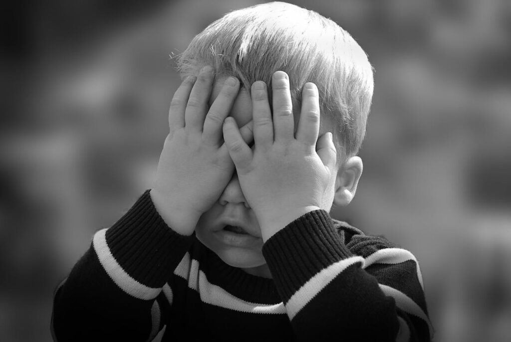 A little boy covering his eyes with his hands, avoiding looking.