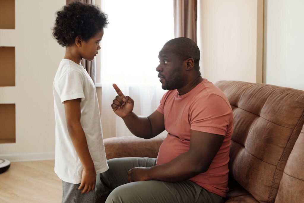 A father scolding his child, pointing a raised finger in a disciplinary gesture.