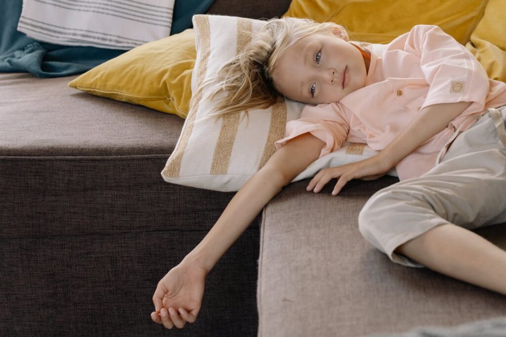 A sad blonde little girl standing on a couch, looking down with a sad expression.