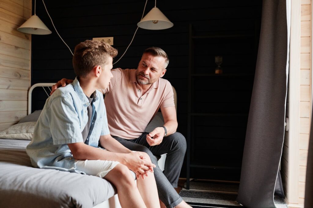 A dad and his teenage son standing on the bed, engaged in a conversation