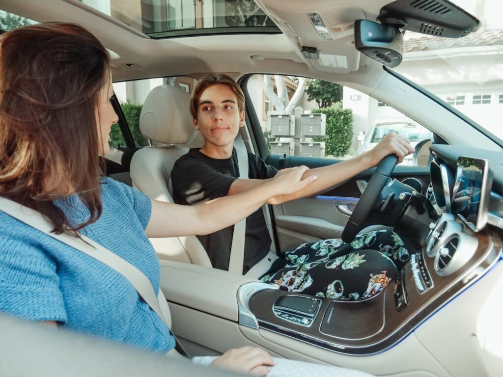 A teenage son driving a car while having a conversation with his mom