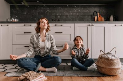 Pacified mom and her little daughter are sitting on kitchen floor and meditate with smile