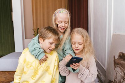 why kids should have phones: 3school-aged children happily gathered around a phone, sharing laughter as they engage with its content